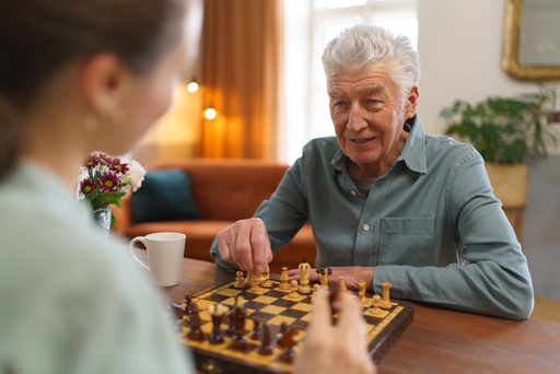 An elderly man playing chess with his live-in carer.