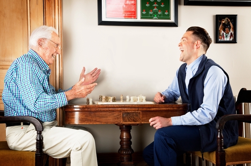A carer and an old man playing chess 