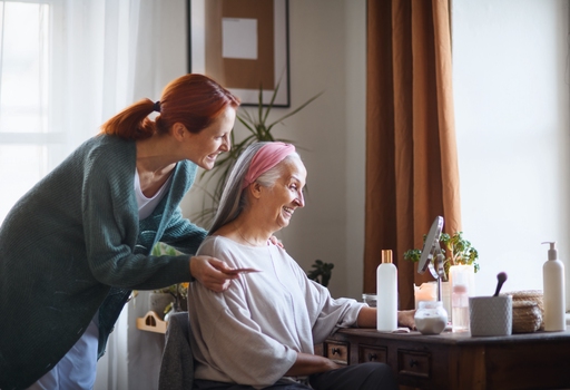 A carer helping an elderly woman with her hair and makeup in front of a mirror