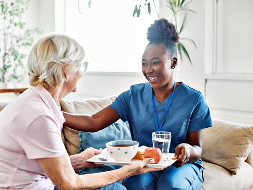 A nurse helping an elderly lady by handing her her breakfast on a tray