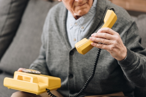 An elderly man holding up a yellow chord phone