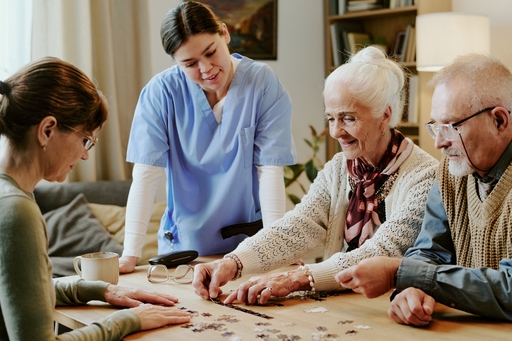 A nurse or carer overlooking some elderly residents doing a jigsaw